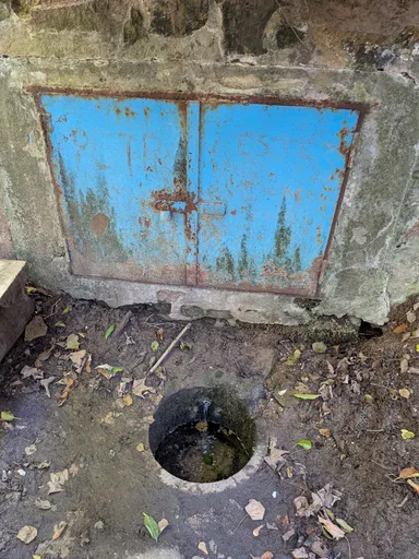 Studánka s modrými plechovými dvířky a otvorem v betonu