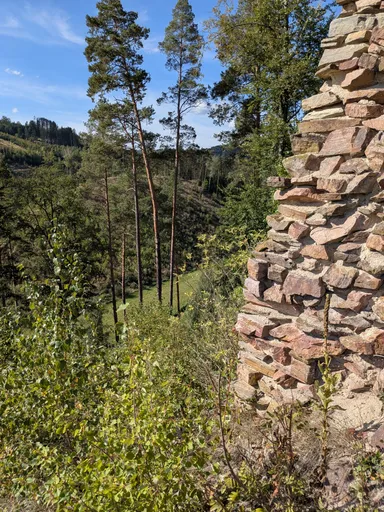 Zbytek kamenné zdi hradní věže mezi stromy, dole zelené údolí.