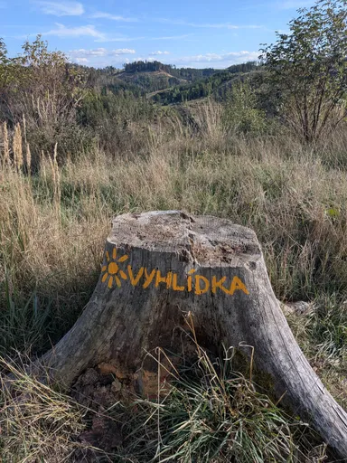 Na pařezu je oranžovým nápisem vyvedeno VYHLÍDKA se sluníčkem.
