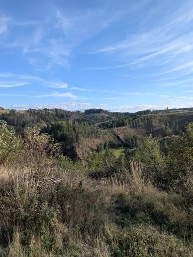 Široký výhled přes údolí na zvlněnou zalesněnou krajinu pod modrou oblohou.