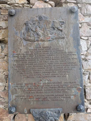 Kovová deska s reliéfem jezdce a rytým textem zasazená do kamenné zdi.