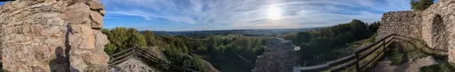 Široké panorama z hradu mezi dvěma kusy zdiva, dole zalesněné údolí a krajina k obzoru.