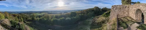 Panorama z hradu přes příkop a zalesněné svahy na širokou krajinu.