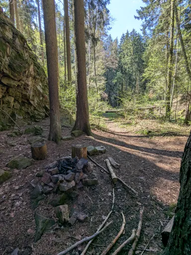Lesní pěšina s kamenným ohništěm pod skalou