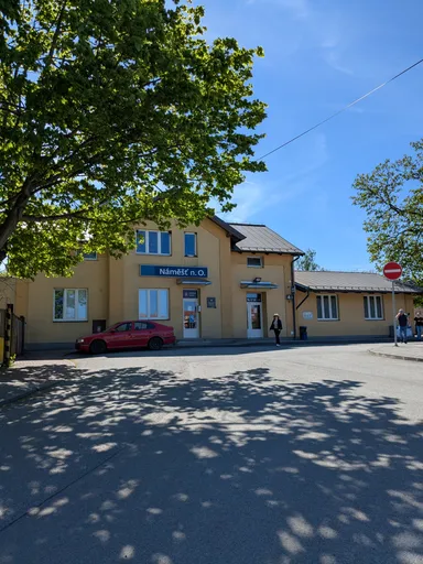 Nádražní budova v Náměšti nad Oslavou se zaparkovaným autem za slunečného jara.