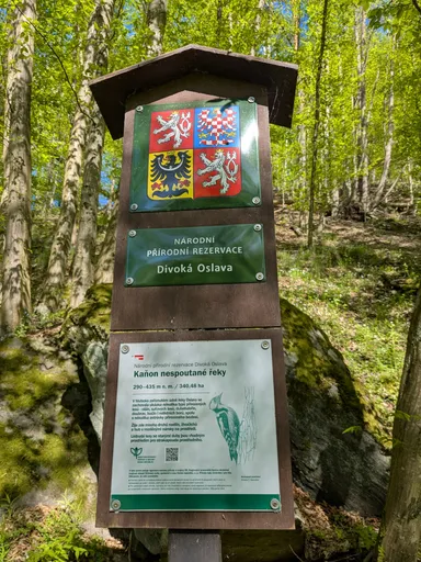 Sloup s tabulí Národní přírodní rezervace Divoká Oslava a státním znakem v jarním lese.