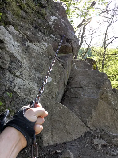 Ruka v rukavici drží řetěz natažený po skále, po kterém se leze nahoru.