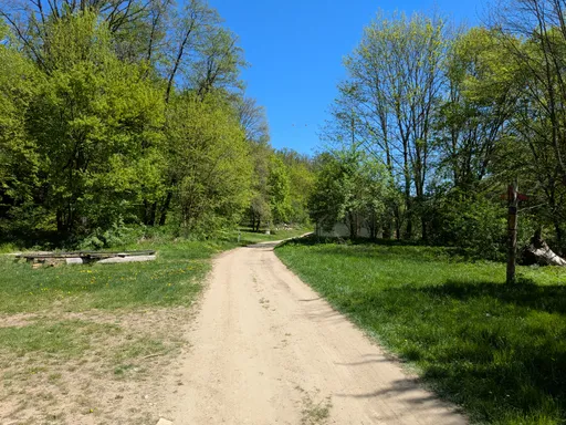 Polní cesta vede jarní loukou v údolí mezi svěže zelenými stromy.