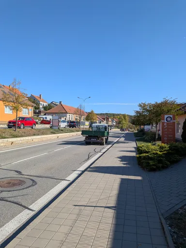 Chodník podél hlavní silnice v Náměšti nad Oslavou za slunečného podzimního dne.