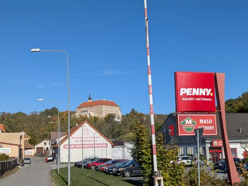 Ulice s prodejnou Penny a řeznictvím, nad střechami se zvedá zámek Náměšť nad Oslavou.