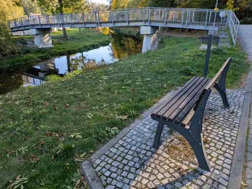 Dřevěná lavička na břehu Oslavy s výhledem na lávku pro pěší přes řeku.