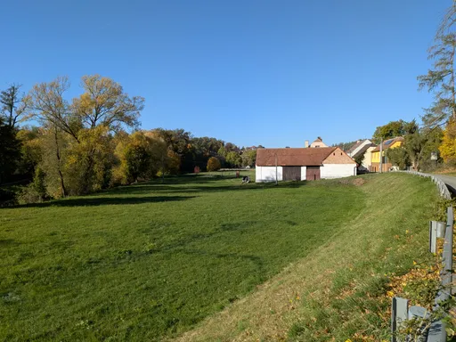 Rozlehlá zelená louka s bílým statkem a podzimními stromy na okraji Náměšti nad Oslavou.
