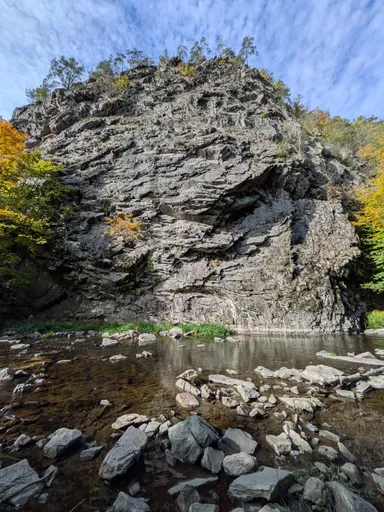 Velký skalní balvan nad kamenitým korytem řeky Oslavy pod modrou oblohou.