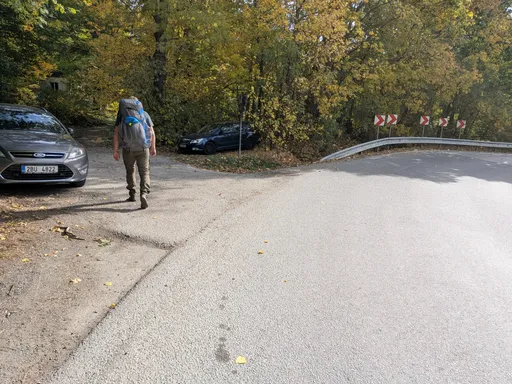 Trempa s batohem jde po silnici kolem zaparkovaných aut směrem k mostu.