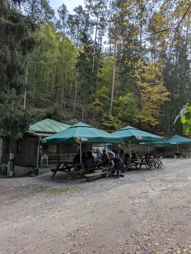 Senoradská kantýna, venkovní posezení pod zelenými slunečníky na okraji lesa.